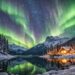 Northern Lights over snowy mountains and cabin by a lake