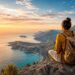 Solo traveler overlooking mountains and ocean at sunrise during a world adventure journey.