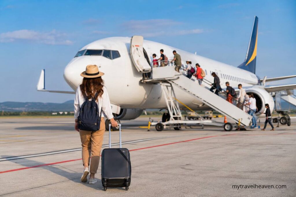 Traveler boarding a budget airline flight at the airport with a suitcase and passengers using boarding stairs under a clear sky.