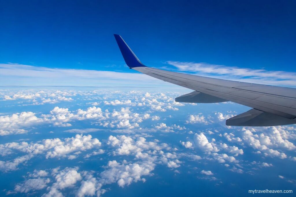 Airplane wing flying above a sea of clouds at cruising altitude under a clear blue sky, illustrating flight levels used by pilots.